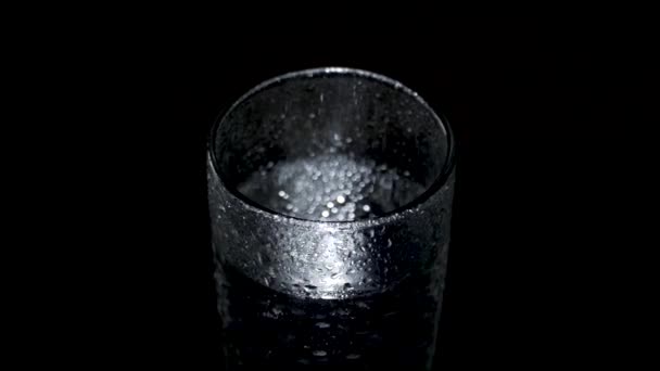 A wet glass of water spins in the dark and approaches — Stock Video