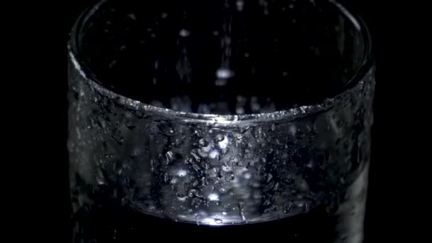 Un vaso de vidrio húmedo de agua gira en la oscuridad y la luz brilla en gotas — Vídeo de stock