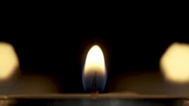 Kamera karanlıkta yanan bir mumun sessiz alevine yakınlaşıyor.