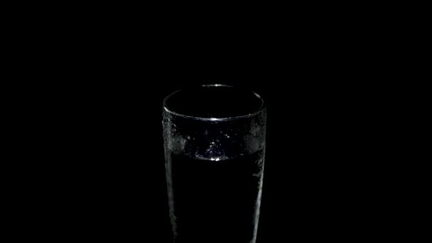 A wet glass of water rotates in the dark in light light — Stock Video