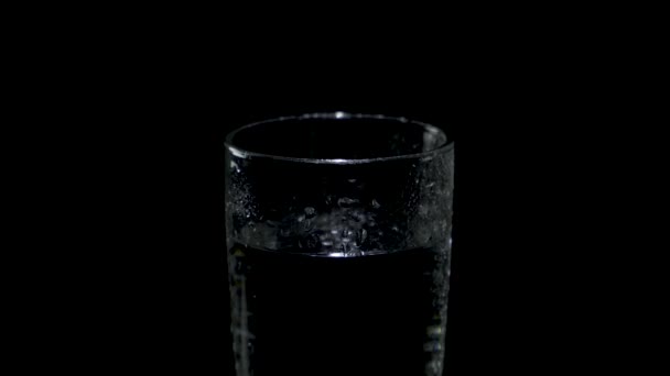 Een glas water dat in het donker ronddraait, verschijnt van onderen. — Stockvideo