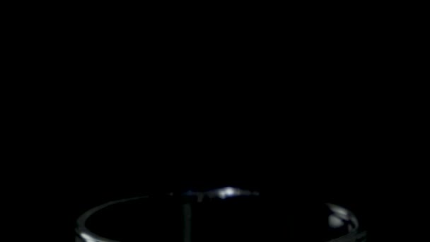 Ett glas vatten snurrar i mörkret framträder underifrån — Stockvideo