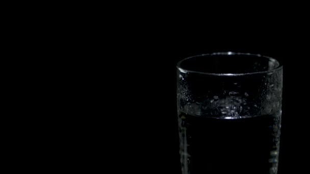 A wet glass of water located on the right side of the screen rotates in the dark — Stock Video