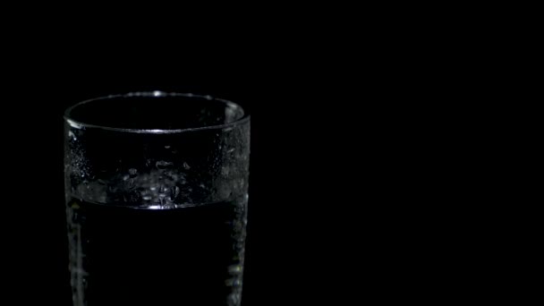Een nat glas water aan de linkerkant van het scherm draait in het donker — Stockvideo