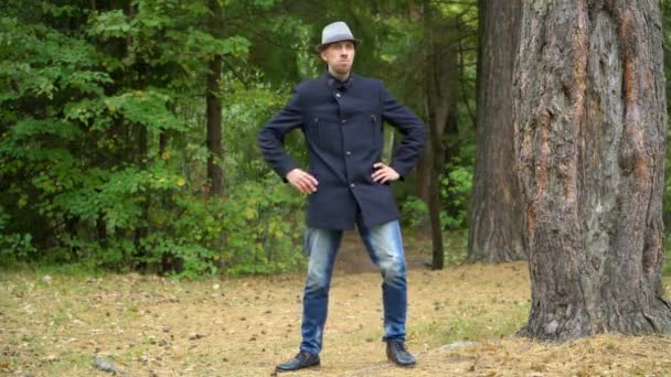 Un uomo d'affari con cappello e cappotto nel bosco si muove felicemente ruotando la mano — Video Stock