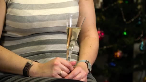 Una chica con una copa de champán en el fondo de un árbol de Navidad — Vídeo de stock