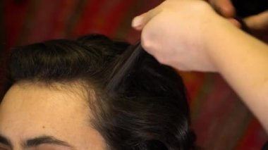 Kuaför bir saç telini saç maşasına takar.
