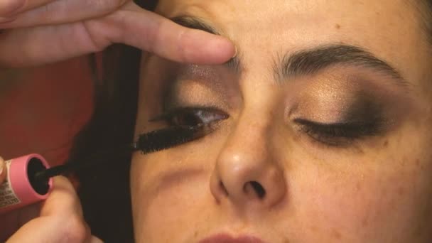 Maskenbildnerin trägt Wimperntusche auf die oberen Wimpern eines Mädchenmodels auf — Stockvideo