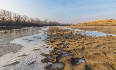 Donmuş nehir ve buz ile kış manzarası kum tepeleri, soğuk güneşli bir günde kaplı.