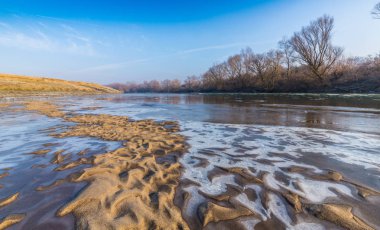 Donmuş nehir ve buz ile kış manzarası kum tepeleri, soğuk güneşli bir günde kaplı.