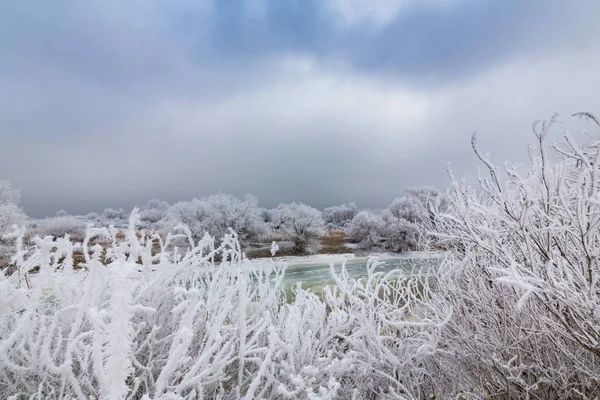 Schöne Winterlandschaft mit Bäumen, die vom Frost bedeckt sind, entlang des gefrorenen Flusses und Gewitterwolken — Stockfoto