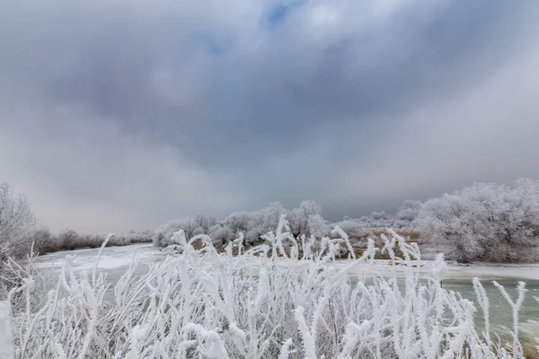 Beautiful winter scenery with trees covered by frost, along frozen river, and storm clouds — Stock Photo, Image