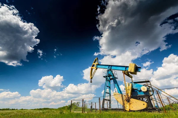 Operating oil and gas well in European oil field, profiled on blue sky with cumulus clouds, in spring — Stock Photo, Image
