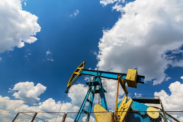 Puits de pétrole et de gaz en exploitation dans le champ pétrolier européen, profilés sur ciel bleu avec cumulus, au printemps — Photo