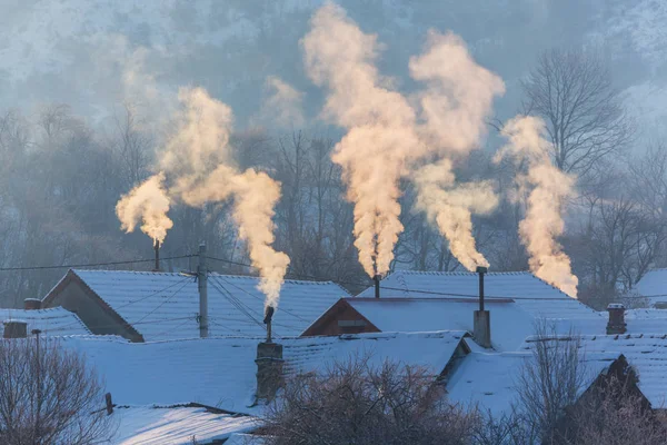 Wunderschöne winterliche Landschaft mit Rauch, der aus den Schornsteinen eines Hauses quillt, an einem hellen, kalten Morgen in einer abgelegenen Landschaft in Europa Stockbild