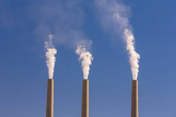 Heavy smoke from coal-powered power plant stacks, profiled on blue sky