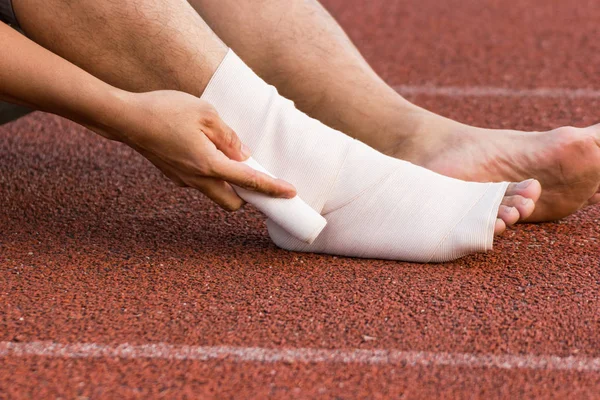 Male athlete applying compression bandage onto ankle injury of a football player, Sports injuries.
