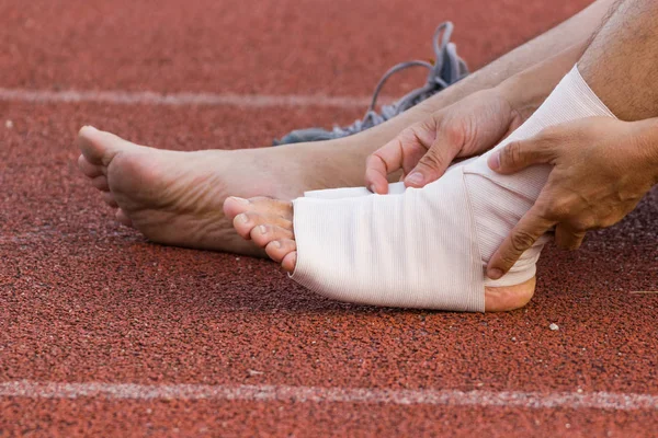 Male athlete applying compression bandage onto ankle injury of a football player, Sports injuries.