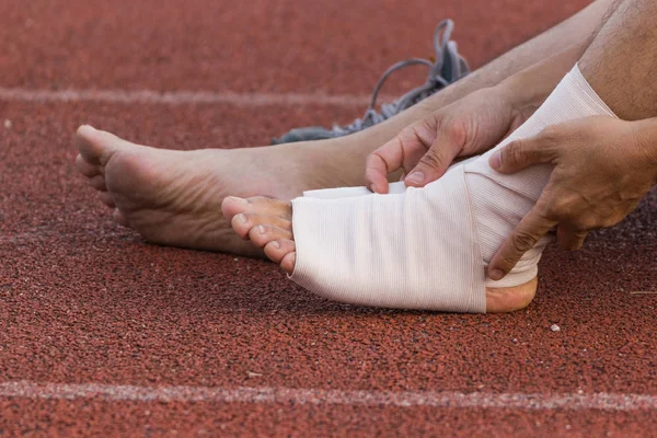 Male athlete applying compression bandage onto ankle injury of a football player, Sports injuries.