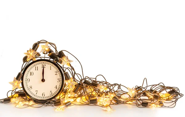 Reloj despertador de Año Nuevo envuelto en una guirnalda de estrellas festivas sobre fondo blanco. Medianoche . — Foto de Stock