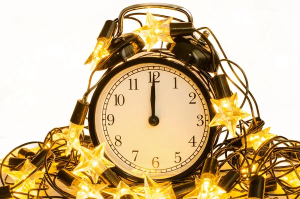 Nieuwjaar wekker verpakt in feestelijke ster slinger op witte achtergrond. Middernacht. — Stockfoto