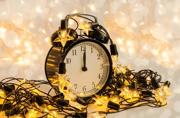 Reloj despertador de Año Nuevo envuelto en una guirnalda de estrellas festivas. Medianoche . — Foto de Stock