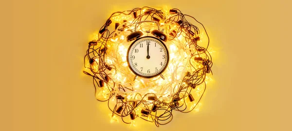 New Year alarm clock surrounded with festive star garland on yellow background. — Stock Photo, Image