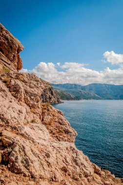 Rocky Coast, dağlar, mavi deniz ve beyaz bulutlu gökyüzü. Dikey fotoğraf.