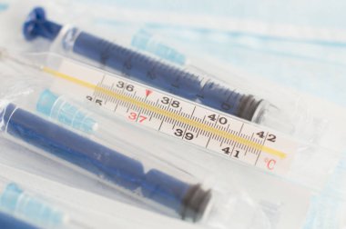 Steril tıbbi maskeler, şırıngalar, aşı şişeleri ve beyaz arka planda analog termometre. Grip mevsimi konsepti. Salgın hastalıkları önleme kavramı.