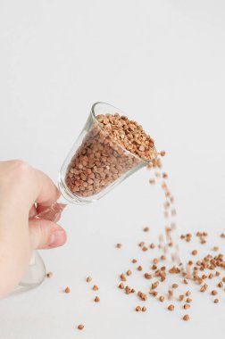 Beyaz arka planda küçük bir bardak karabuğday - geleneksel Rus yemeği - saçılan bir el. Karabuğday eksikliği kavramı.