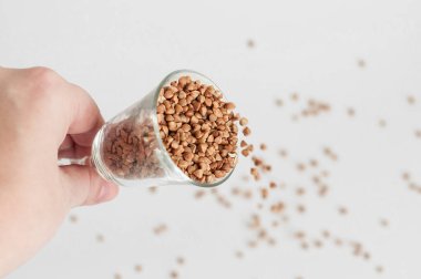 Beyaz arka planda küçük bir bardak karabuğday - geleneksel Rus yemeği - saçılan bir el. Karabuğday eksikliği kavramı.