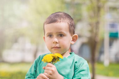 Güneşli bir günde elinde sarı karahindiba tutan yeşil elbiseli küçük bir çocuk..