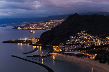 Alacakaranlık arka plan, ön plan ve Kuzey Atlantik Okyanusu Las Teresitas Beach'te soldaki şehir Santa Cruz de Tenerife ile güzel aydınlatılmış San Andres şehir görünümünü