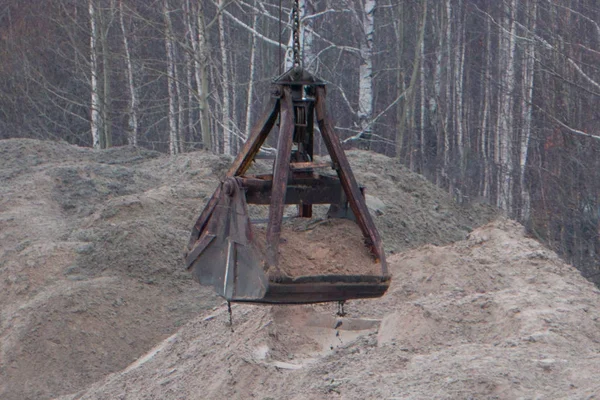 Grúa de construcción. Grúa de construcción con un cubo parado cerca de la pila de arena  . — Foto de Stock