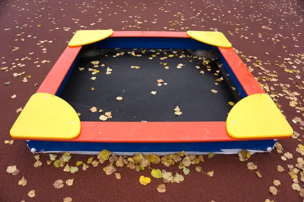 Sandpit, on a red background with fallen leaves . — Stock Photo, Image