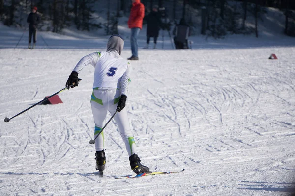 Hübsche junge Skirennläuferin in einem weißen Ensemble aus Skianzug, Skiern, Stöcken und Helm posiert auf einem Bergskigebiet im frischen weißen Winterschnee . — Stockfoto