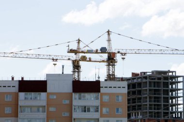 Açık mavi gökyüzü ve güneşli bir bina kompleksi üzerinde çalışan birkaç vinç de dahil olmak üzere büyük bir inşaat sahası. .