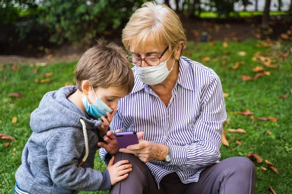 外婆家和小孩在后院玩智能手机时戴着防毒面具 免版税图库图片
