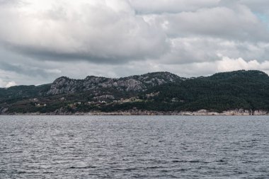 Norveç 'in kasvetli bir gününde Bjarnafjorden sularının kıyısındaki dağ sırtlarındaki evler