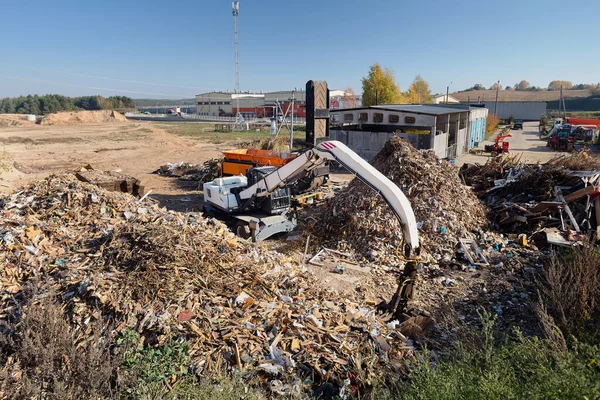 Excavator and shredder designed for pre-processing of materials municipal waste and construction debris roots workes on waste recycling plant grinding pile of wood waste for processing and recycling