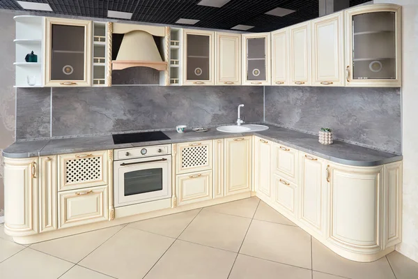 Interior of modern kitchen in classic style with golden elements in beige colors with built-in appliances electric or induction hob, electric oven stone sink and extractor fan