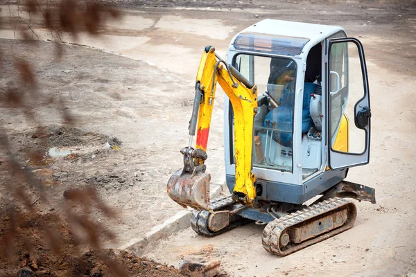 Tracked mini excavator breaks out old curbs before installing new curbs. The concept of using economical and compact equipment for urban needs.