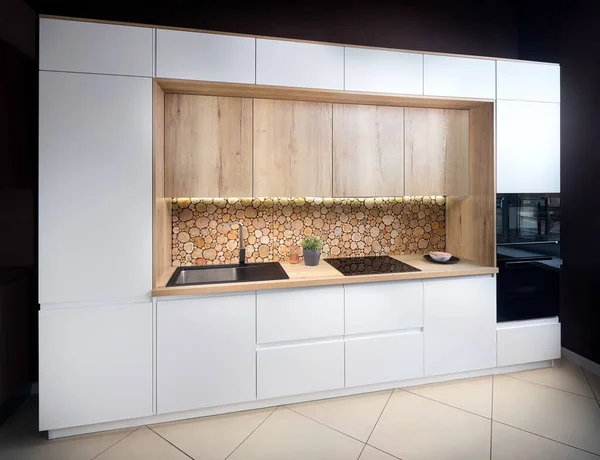 Luxury modern fitted flat design kitchen with surface behind the countertop decorated with wall cross section of tree trunks of cut tree logs, trunks placed together for interior decoration