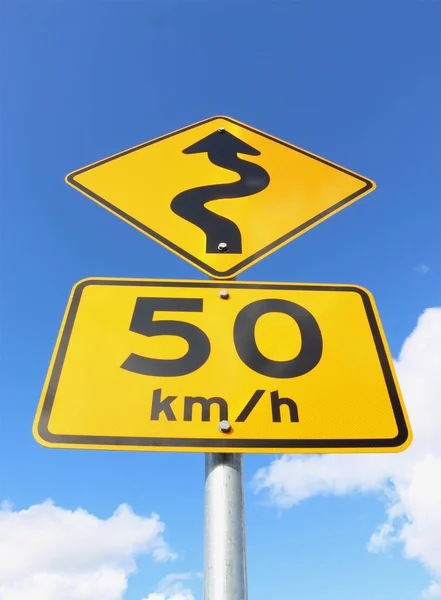 Un segnale limite di velocità nero e giallo 50 km / h su strada ventosa con freccia in un cielo blu — Foto Stock