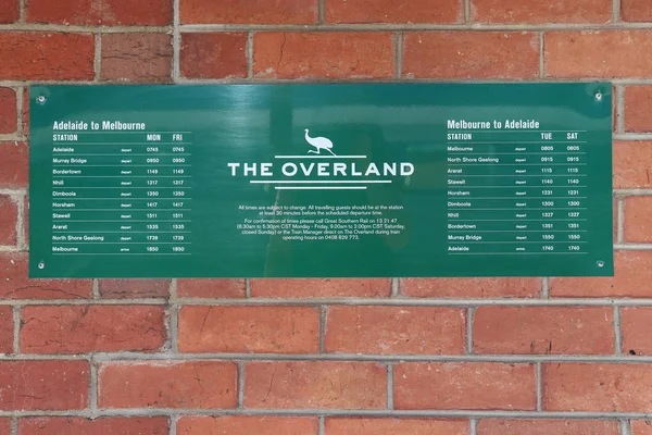 Muro de ladrillo rojo con letrero verde y blanco que indica las horas de llegada y salida del tren de Overland — Foto de Stock