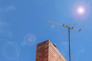 Bir analog televizyon anteni, mavi gökyüzünde, kırmızı tuğlalı bir bacada, mercekli.