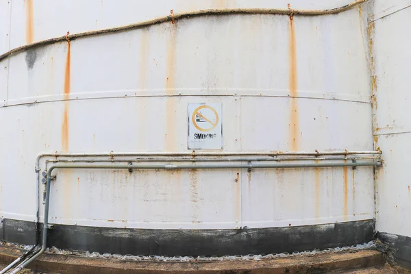 A weathered Smoking Prohibited sign on the exterior of an old disused fuel storage tank — Stockfoto