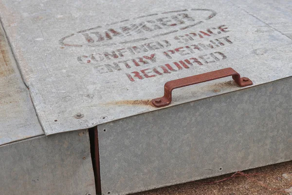 a faded Danger, Confined Space Entry Permit Required warning sign on the uplifing door of an inground grain storage bin