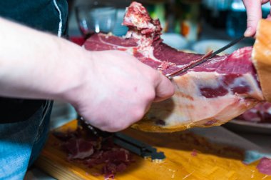 Kasap, kırmızı şarap kadehinin yanında parti için jamonu bıçakla keser.