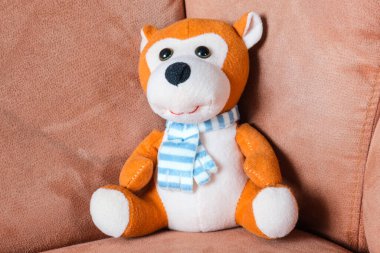 yumuşak turuncu beyaz oyuncak kırmızı koltukta oturuyor.